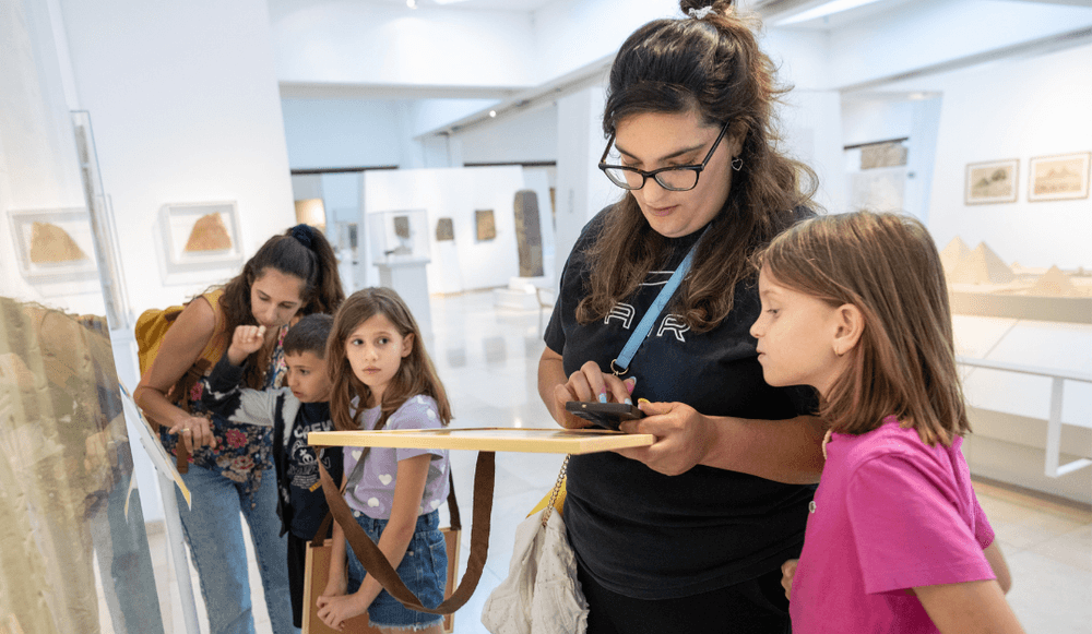 מדריכה במוזיאון מסייעת לילדים לחקור מיצג אינטראקטיבי במהלך פעילות הקיץ.