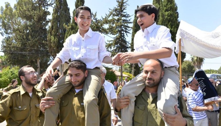 Bar-Mizwa-Feier in Jerusalem mit zwei Jungen, die während einer traditionellen Prozession auf den Schultern getragen werden, umgeben von Familie, Freunden und Soldaten.