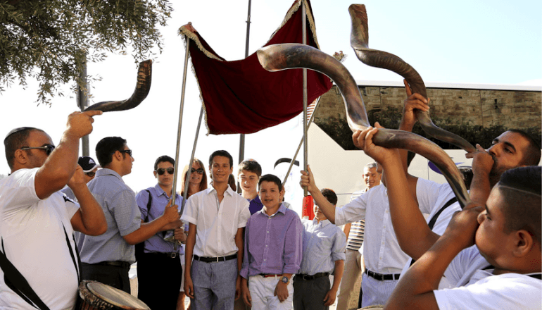 Celebración de Bar Mitzvah en Israel con niños pequeños bajo un dosel mientras los músicos tocan shofars en una procesión festiva.